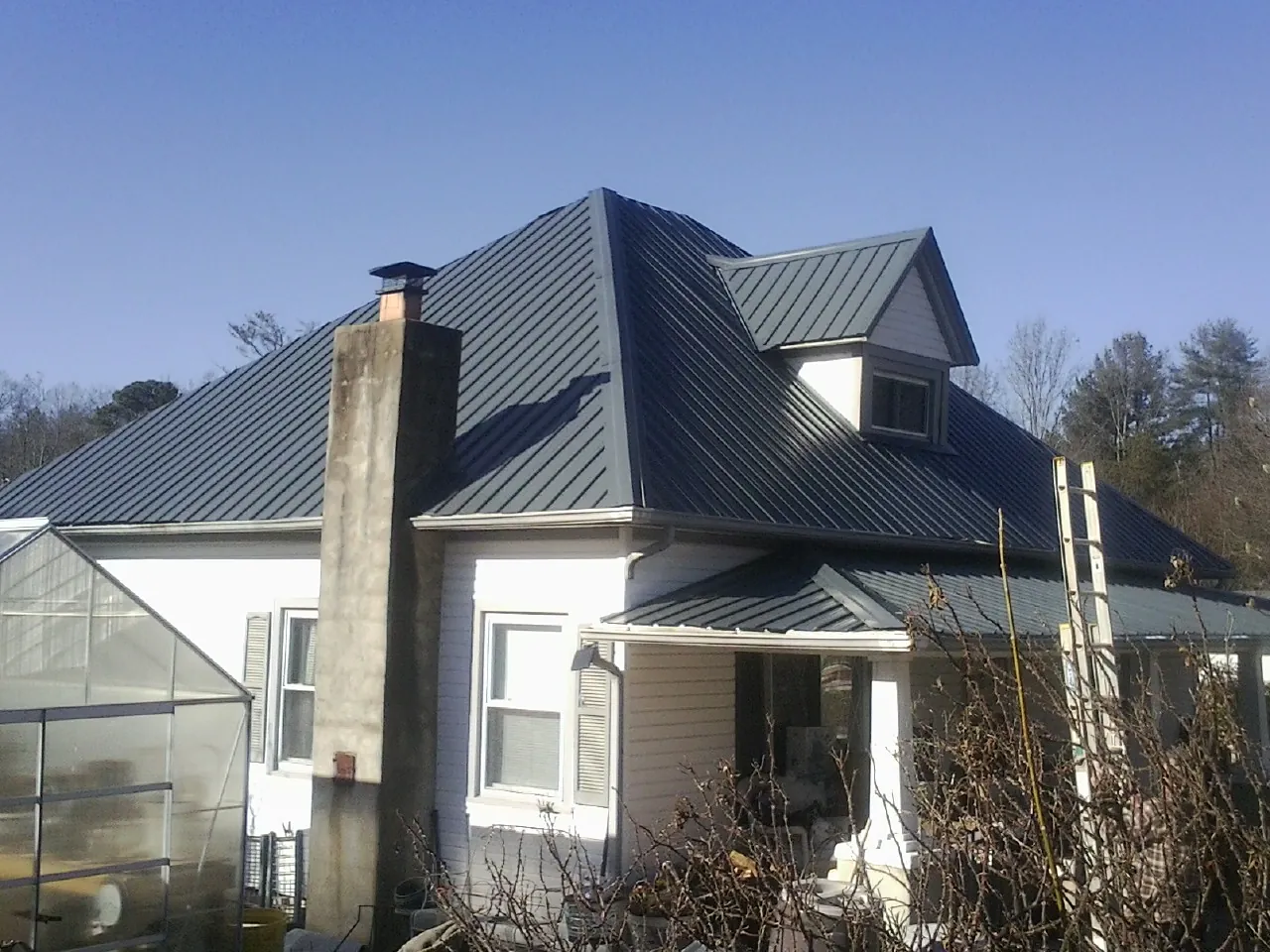 Dark blue standing seam metal roof on a white farmhouse with dormer — Slate & Tile Roof Repair by Roofing Brothers in Jud