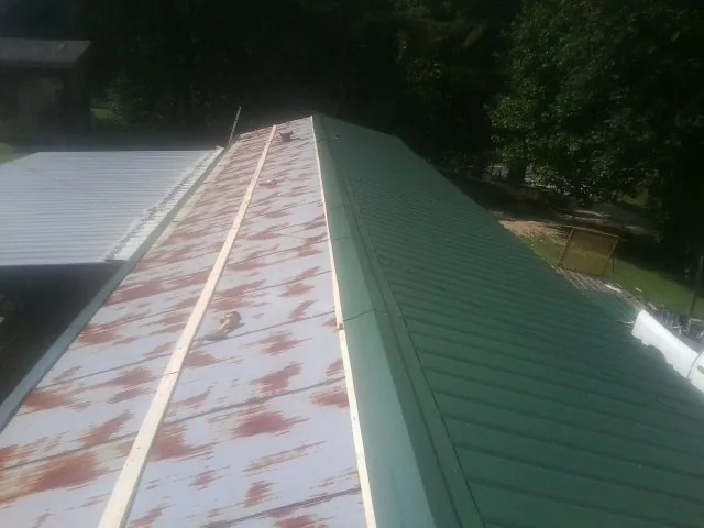 Old rusted panels beside newly installed green metal roofing — Wind Damage Roof Repair by Roofing Brothers in Jud