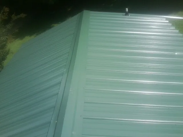 New green metal panels meeting at the ridge of a roof — Flat Roof Repair work by our crew in Jud