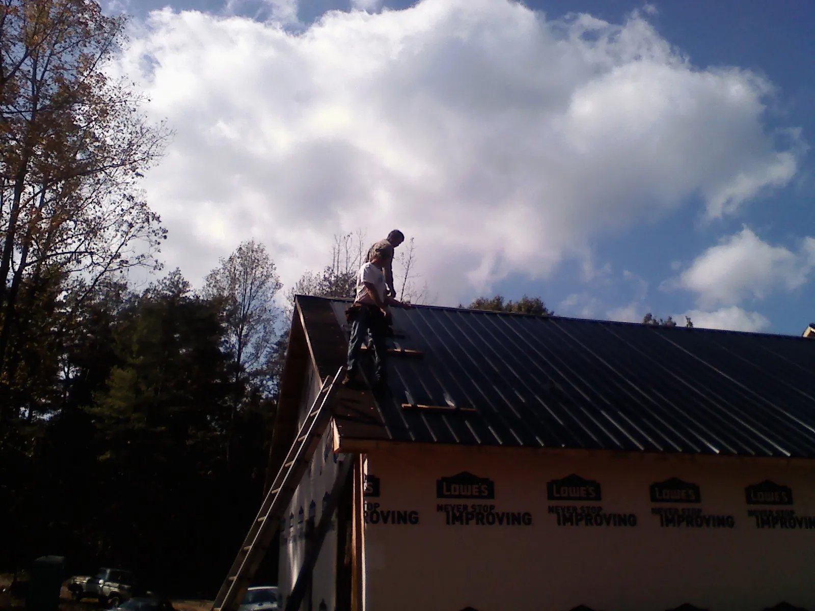 Roofer fastening dark metal panels high against a cloudy sky, from a Roof Inspection job in Jud