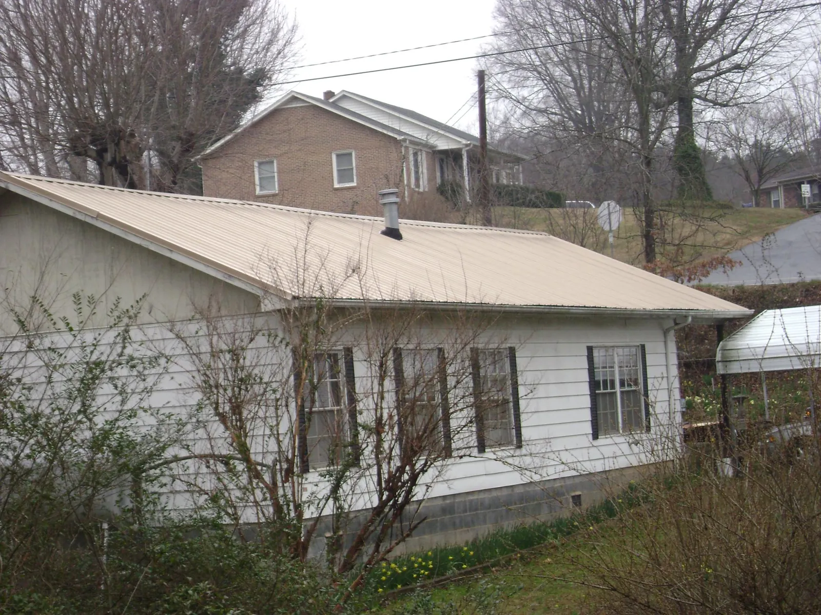 Tan metal roof on a white sided house set into a hillside — Commercial Roofing by Roofing Brothers in Jud
