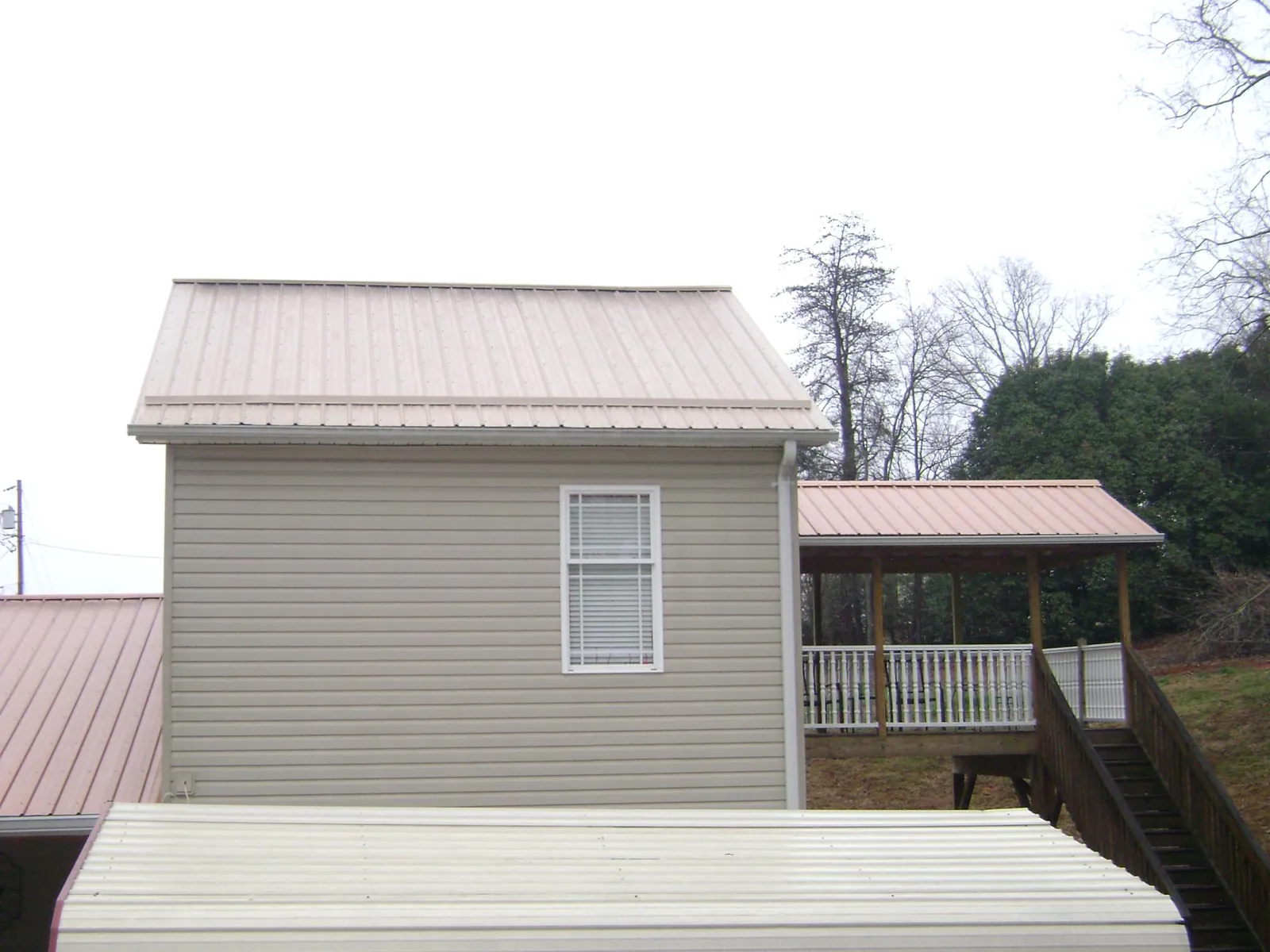 Tan metal roofs on a two story addition and attached porch, from a Roof Replacement job in Jud